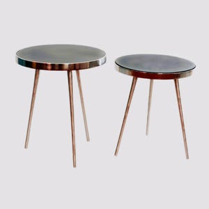 May include: Two round side tables with dark, reflective circular tops and thin, metallic tripod legs. The tables are of different heights, with the larger table on the left and the smaller table on the right, both featuring a sleek, simple design.