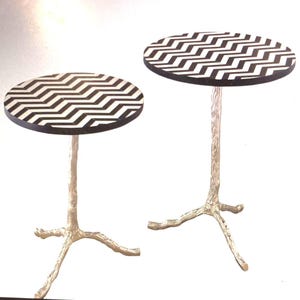 May include: Two round side tables with black and white chevron patterned tops and silver tree branch-like legs.