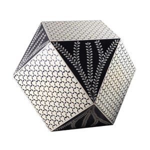 May include: A geometric decorative object with a multifaceted design. The object features a combination of black and off-white panels. Some panels have a star pattern, others have a leaf design, and some are solid black.