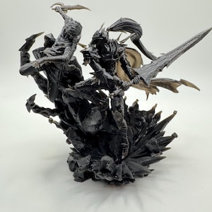 May include: Black and silver detailed figurine of two figures in a battle pose. The figures are standing on a rocky base with sharp edges.