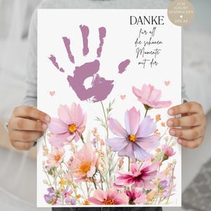 Może przedstawiać: Grafika z fioletowym odciskiem dłoni i niemieckim tekstem, w tym słowem "DANKE". Projekt zawiera akwarelowe kwiaty w odcieniach różu, fioletu i żółci. Małe różowe serca są rozrzucone po grafice, w formacie DIN A4.