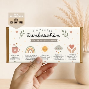 Può includere: Una barretta di cioccolato con la scritta "Ein kleines Dankeschön" e "Für die beste Erzieherin". La barretta presenta illustrazioni di una tazza, un arcobaleno, un sole, una nuvola e un cuore. La barretta è tenuta in mano.