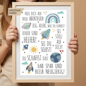 Puede incluir: Una impresión enmarcada con un marco de madera clara. La impresión presenta una colorida ilustración de un arcoíris, cohetes, planetas y estrellas. El texto en alemán dice "FREU DICH AUF NEUE ABENTEUER!" y otras frases motivadoras.