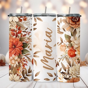 May include: Three cylindrical tumblers with lids and straws, featuring a white background decorated with orange, cream, and brown floral illustrations. The center tumbler displays the name Maria in a brown script font, surrounded by autumn-toned leaves.