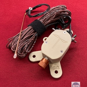 May include: A beige antenna tuner with a copper-colored knob and the text "49:1". It has a black cable and a bundle of brown wire secured with a black strap. A copper-colored antenna is also included.