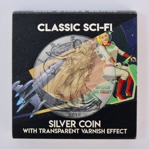 May include: A silver coin with a transparent varnish effect. The coin features a depiction of Lady Liberty and the words "IN GOD WE TRUST" and "2019". The coin is overlaid with a sci-fi image of a woman riding a futuristic motorcycle.