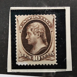 May include: A brown and white 10-cent postage stamp featuring a portrait of Benjamin Franklin. The stamp has a black border and is surrounded by a white border.