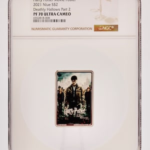 Peut inclure: Une affiche du film Harry Potter et les Reliques de la Mort, partie 2, classée dans un boîtier en plastique. L'affiche présente une image sombre d'Harry Potter et d'autres personnages devant un bâtiment. L'affiche est classée PF 70 ULTRA CAMEO par la Numismatic Guaranty Corporation.