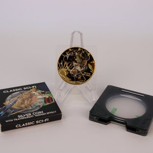 May include: A gold-colored coin with a black and gold design featuring a space scene. The coin is on a clear plastic stand. The coin is packaged in a black box with the text "CLASSIC SCI-FI SILVER COIN WITH TRANSPARENT VARNISH EFFECT CLASSIC SCI-FI" printed on it.