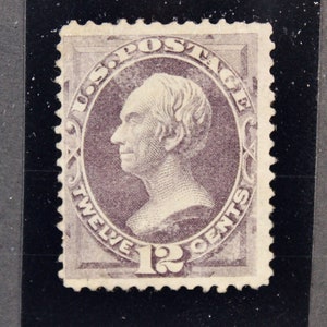 May include: A vintage 12-cent postage stamp featuring a portrait of Benjamin Franklin in a purple color scheme. The stamp has a decorative border with the words "U.S. Postage" and "Twelve Cents".