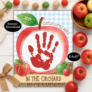May include: A digital print featuring a red apple design with a handprint, the text "Cutest Little Apple In The Orchard", and the year 2025. The print measures 21.6 x 27.9 cm. Includes a bowl of apples.