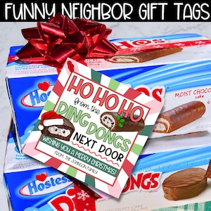 May include: A gift set featuring Hostess chocolate cakes with a red bow and a gift tag. The tag reads "HO HO HO from the DING DONGS NEXT DOOR" with a Christmas theme and the text "WISHING YOU A MERRY CHRISTMAS!"