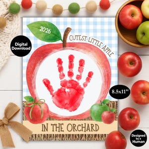 May include: A digital download print featuring a large red apple illustration with a white center containing a red handprint. The text reads 2026, Cutest Little Apple, and In The Orchard. The background is a light blue gingham pattern, 8.5x11 inches.