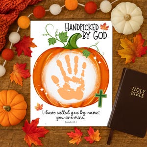 May include: A seasonal print with an orange pumpkin design and the text "HANDPICKED BY GOD." The image includes a Bible, autumn leaves, and the Bible verse Isaiah 43:1. The theme is religious and autumnal, perfect for fall.