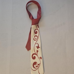 May include: A white tie with a burgundy floral pattern. The tie has a burgundy colored back.