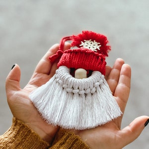 May include: A white and red crocheted gnome ornament with a white tassel beard and a red hat with a snowflake on top.