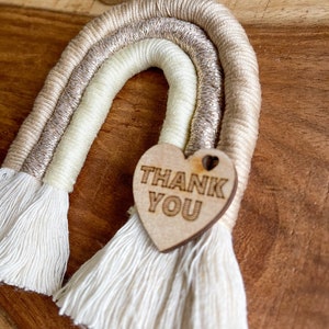 May include: A beige, white and gold rainbow wall hanging with a wooden heart that says "Thank You".