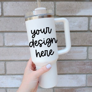 May include: White stainless steel travel mug with a handle and a black inscription that says "your design here".