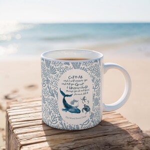 Könnte beinhalten: Eine weiße Keramiktasse mit einem blauen und weißen Design, das eine Wal, einen Oktopus und eine Schildkröte zeigt. Die Tasse trägt den Text "Call to Me and I will answer you and tell you Great & Unsearchable things you do not know. Jeremiah 33:3" und "The Word Sown Deep".
