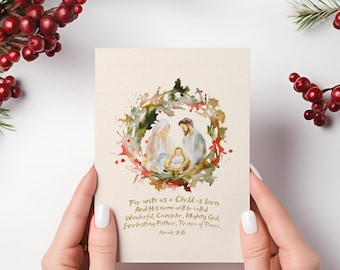May include: A cream-colored Christmas card featuring a watercolor illustration of the Nativity scene within a wreath of greenery and red accents. The card includes text from Isaiah 9:6.