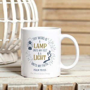 May include: White ceramic mug with a curved handle. The mug features a design with the text "THY WORD IS A LAMP UNTO MY FEET & A LIGHT UNTO MY PATH. PSALM 119:105 The Word Sown Deep". The design includes a lantern and footprints.
