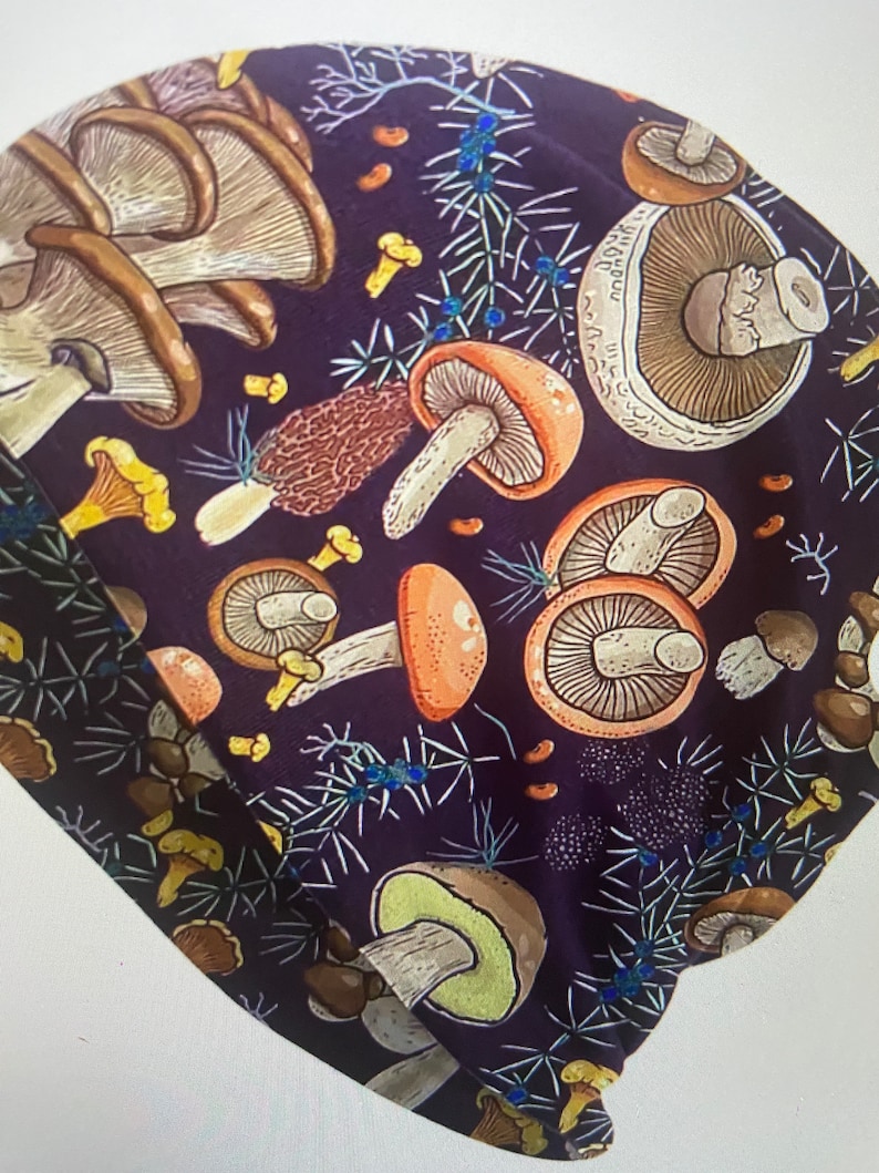 Puede incluir: Una tela de color morado oscuro con un patr&oacute;n repetido de setas y agujas de pino. Las setas son de varios colores, incluyendo marr&oacute;n, naranja y blanco. Las agujas de pino son verdes y marrones.