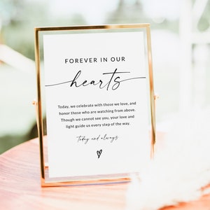 May include: A gold-framed sign with a white background and black text that reads "FOREVER IN OUR hearts Today, we celebrate with those we love, and honor those who are watching from above. Though we cannot see you, your love and light guide us every step of the way. Today and always ♡".