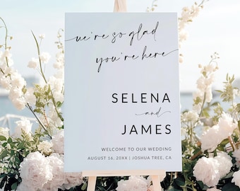 Peut inclure: Une pancarte de bienvenue de mariage blanche avec du texte en calligraphie noire qui dit "we're so glad you're here" et "Selena and James". La pancarte indique également la date et le lieu du mariage : "August 16, 20XX | Joshua Tree, CA".