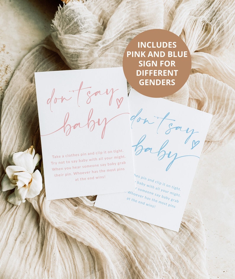 May include: Two signs with the text "don't say baby" in pink and blue. The signs are on a beige fabric background. The text "Includes pink and blue sign for different genders" is on a brown rectangle.