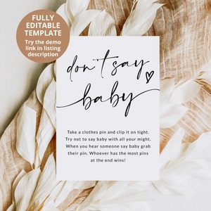 May include: A white card with black text that says "don't say baby" with a heart symbol. The card has instructions for a game where players try not to say the word "baby" and whoever has the most clothes pins at the end wins.