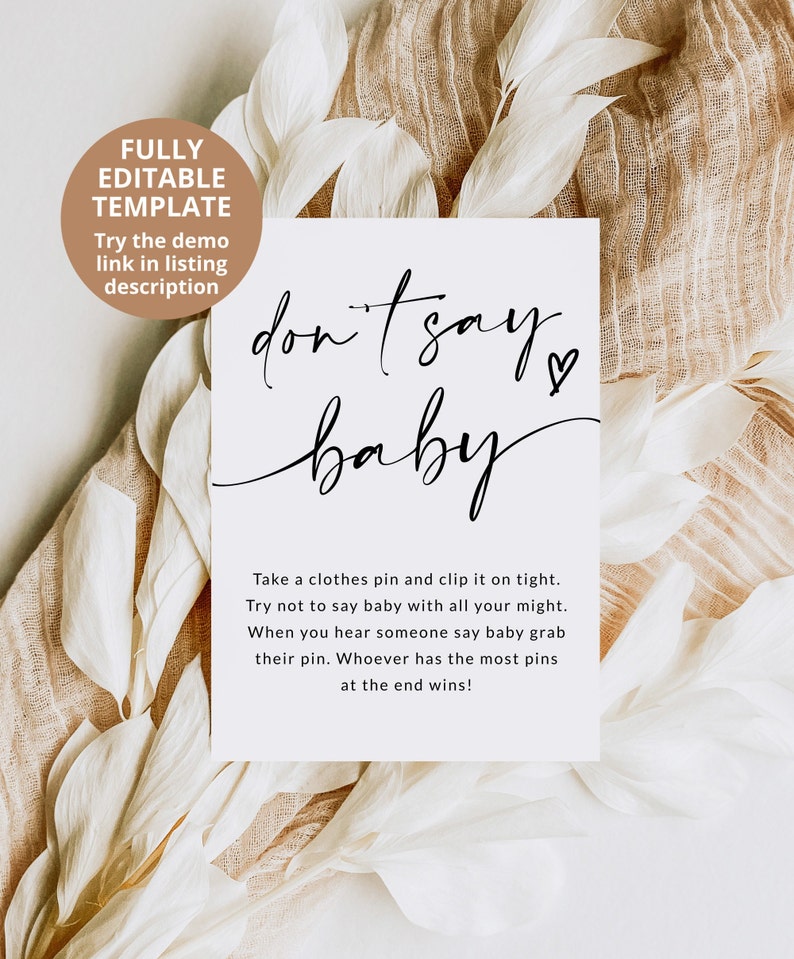 May include: A white card with black text that says "don't say baby" with a heart symbol. The card has instructions for a game where players try not to say the word "baby" and whoever has the most clothes pins at the end wins.