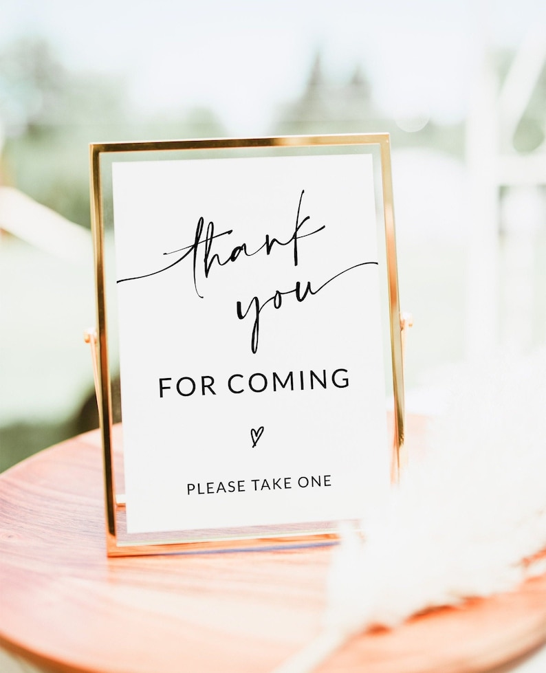May include: A gold-framed sign with white background and black calligraphy that reads "thank you for coming" with a small heart symbol and the text "please take one" below.