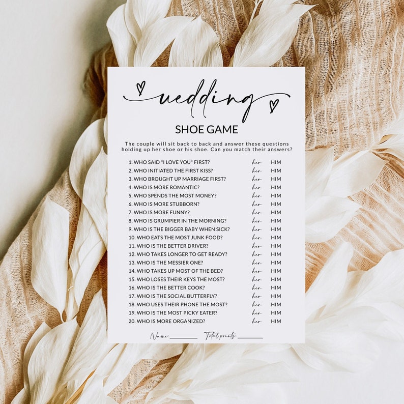 May include: A printable wedding shoe game with 20 questions for the couple to answer. The questions are about who does what more, like who is more romantic, who is more stubborn, who is funnier, who eats the most junk food, who is the better driver, who takes longer to get ready, who is the messier one, who takes up most of the bed, who loses their keys the most, who is the better cook, who is the social butterfly, who uses their phone the most, who is the pickiest eater, and who is more organized. The game includes a space for the couple's names and total points.