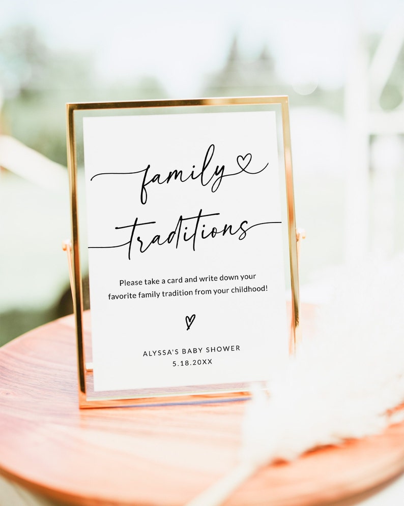 May include: A gold-framed sign with white background and black text that reads "family traditions". The sign also includes the text "Please take a card and write down your favorite family tradition from your childhood!" and "ALYSSA'S BABY SHOWER 5.18.20XX".