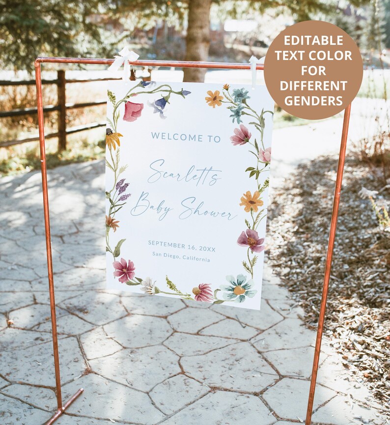 Pu&ograve; includere: Un cartello rettangolare bianco appeso a una cornice in metallo color rame, caratterizzato da un bordo floreale ad acquerello con fiori blu, rosa, gialli e verdi. Il testo recita: Welcome to Scarlett's Baby Shower, September 16, 20XX, San Diego, California.