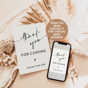 May include: Two printable thank you cards for a virtual baby shower. The cards are white with black text that says "thank you for coming" and a heart symbol. The cards also say "Please take one". The cards are on a light brown background with dried palm leaves and white coral.