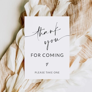 May include: White card with black calligraphy that says "thank you for coming" with a heart symbol and the text "please take one" at the bottom. The card is on a white and brown background.