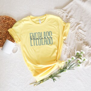 May include: A yellow t-shirt with the text "Eyeglass Dealer" in grey and black lettering. The text includes a pair of eyeglasses.