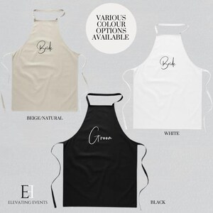 May include: Three aprons in beige, white, and black, each with text. The beige apron says "Bride", the black apron says "Groom", and the white apron says "Bride". Ideal for a wedding or bridal event.