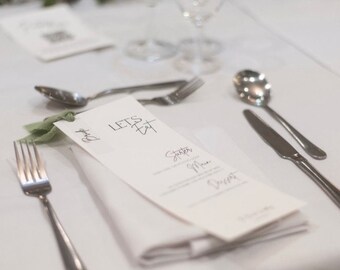 May include: A white table setting with a folded napkin, silverware, and a menu card that says "Let's Eat".