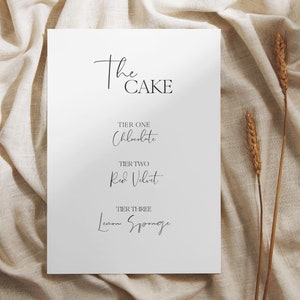 May include: A white card with the text "The Cake" in black script font. The card lists the cake flavors for each tier: Tier One - Chocolate, Tier Two - Red Velvet, Tier Three - Lemon Sponge.