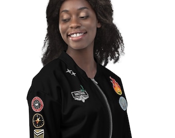 May include: A black bomber jacket with a zipper closure and multiple patches on the sleeves. The patches include a compass, a star, a plane, and a fire design. The jacket is worn by a person with dark hair.