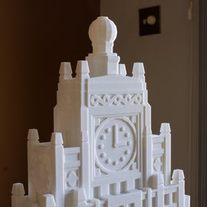 May include: A white, detailed model of a clock tower with a domed roof and a clock face with Roman numerals.