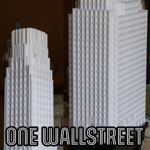 Könnte beinhalten: Zwei weiße Modellgebäude von Wolkenkratzern, eines größer als das andere. Das größere Gebäude trägt den Text "ONE WALL STREET" auf dem Sockel.