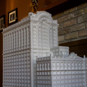 May include: A white model of a tall building with many windows and intricate details. The model is made of a smooth, white material and appears to be a replica of a real building.