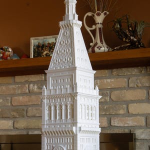 Peut inclure: Modèle 3D imprimé en blanc d'un immeuble haut avec un cadran d'horloge et des détails complexes. Le modèle est sur une étagère devant un mur en briques.
