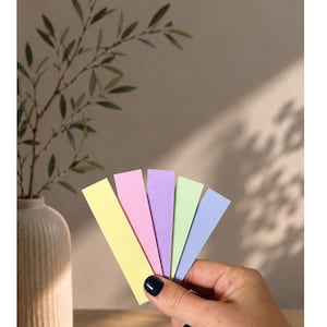 May include: Five rectangular paper strips in pastel colors: almond yellow, pink, lilac, mint green, and pale blue. The text at the top reads: Unsere Pastellfarben. Below, the text lists: MANDELGELB - ROSA - FLIEDER - MINTGR&Uuml;N - LILABLASSBLAU.