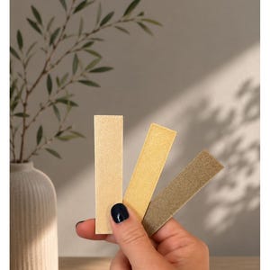 May include: Three rectangular swatches in varying metallic shades of light gold, yellow gold, and old gold. The text above the swatches reads "Unsere Goldt&ouml;ne" followed by "LIGHTGOLD - GELBGOLD - OLDGOLD" in black capital letters.