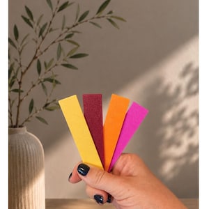 May include: Four rectangular strips in mustard yellow, dark red, orange, and magenta. The text at the top reads "Unsere Knalligen I" followed by "SENFGELB - DUNKELROT - ORANGE - MAGENTA". The strips are held in a fan shape against a neutral background.