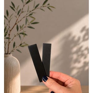 May include: Two rectangular black strips with a textured surface. The text "Unsere Darks" and "SCHWARZ - GRAHIT (SCHIMMERND)" appears at the top of the image. The strips have a matte finish and are held together in a vertical orientation.
